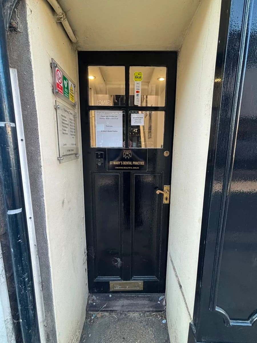 The black front door of St Mary's Dental Practice, set back in a narrow alcove, with the practice nameplate and opening times beside it